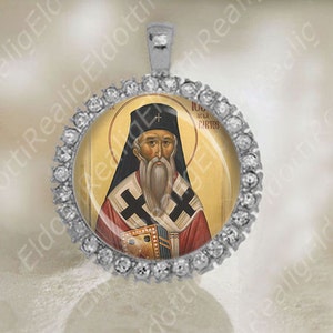 May include: Silver pendant with a round glass insert featuring a religious icon of a bearded man in a red and black robe. The icon is surrounded by a silver frame with small clear rhinestones. The pendant is on a white background.