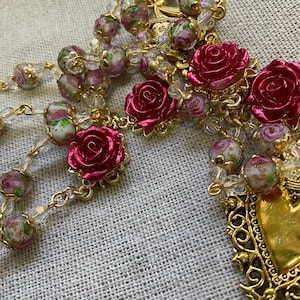 Close-up of red rose Pater beads, crystal floral Ave beads and an ornate gold-tone Sacred Heart devotional medal on a handmade Catholic rosary.