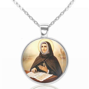 Può includere: Collana d'argento con un ciondolo rotondo di vetro che presenta un dipinto di una donna con abito marrone che tiene una mappa. Il ciondolo ha un bordo argentato.