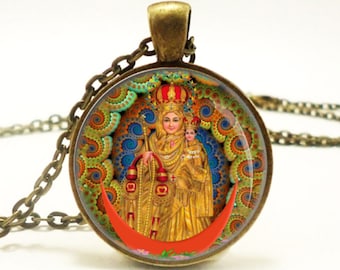 May include: A gold pendant necklace with a round glass charm featuring a colorful image of the Virgin Mary holding a baby Jesus. The charm has a red crescent moon and a swirling mandala-like background.