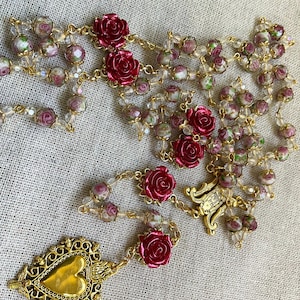 Full view of the handmade red rose rosary arranged on linen, featuring clear pink lampwork beads, gold-tone links, Immaculate Mary and Sacred Heart details.
