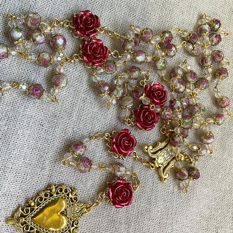 Full view of the handmade red rose rosary arranged on linen, featuring clear pink lampwork beads, gold-tone links, Immaculate Mary and Sacred Heart details.