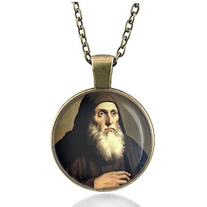 May include: A bronze chain necklace with a round glass pendant featuring a portrait of a man with a long white beard. The man is wearing a brown robe and has a serious expression.