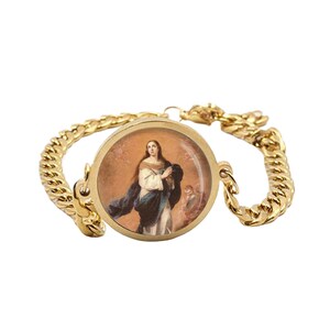 May include: Gold-coloured bracelet with a round pendant displaying a religious painting. The bracelet has a thick chain design and a clasp. The pendant shows a woman in a white and blue robe, with a warm-toned background.