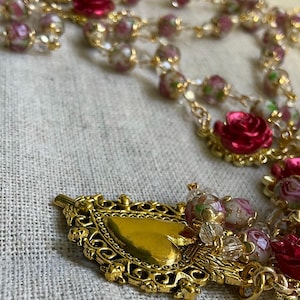 Detail of the gold-tone Sacred Heart of Jesus medal surrounded by floral lampwork glass beads and red rose beads on this handmade Catholic rosary.
