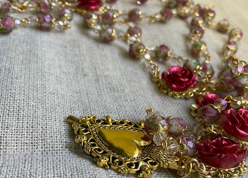 Detail of the gold-tone Sacred Heart of Jesus medal surrounded by floral lampwork glass beads and red rose beads on this handmade Catholic rosary.