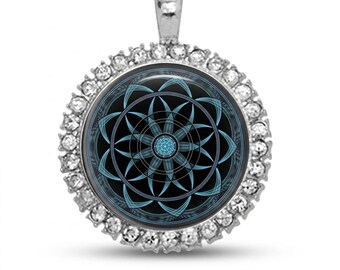 May include: A silver pendant with a round, black center featuring a blue geometric design. The pendant is encircled by a row of clear, sparkling crystals. The bail is also silver. This necklace is a stylish accessory.