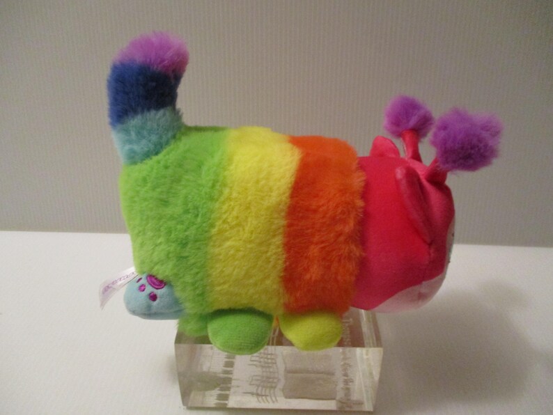 Pu&ograve; includere: Un peluche a forma di bruco con un corpo a strisce arcobaleno caratterizzato da segmenti verdi, gialli e arancioni. La testa &egrave; rosa brillante con due antenne viola soffici. Presenta una coda blu e piccoli piedi azzurri con impronte di zampe.