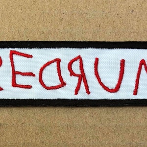 May include: A white patch with a black border, featuring the word "REDRUM" embroidered in red thread.