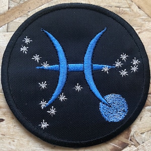 May include: Embroidered black patch featuring the Pisces zodiac symbol in blue, with a constellation of small, silver stars. The patch is circular and has a black border. The Pisces symbol is a pair of curved lines.