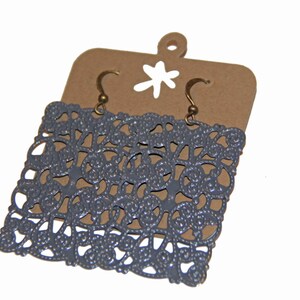 May include: Gray filigree earrings with a square shape and a delicate design. The earrings are hanging on a brown card with a white star.