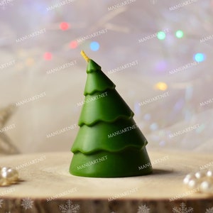 Puede incluir: Una vela de árbol de Navidad verde con una parte superior dorada. La vela está sentada sobre una superficie de madera con cuentas de perlas blancas a cada lado.