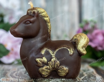 Könnte beinhalten: Eine braune und goldene Kerze in Form eines Pferdes mit einem floralen Design. Die Kerze steht auf einer Holzoberfläche.