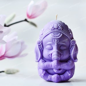 Può includere: Candela viola a forma di elefante in meditazione con un copricapo dettagliato e gli occhi chiusi. La candela è su una superficie bianca.