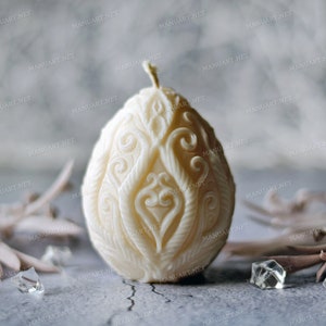 May include: A white egg-shaped candle with an intricate floral design. The candle is made of wax and has a delicate, ornate pattern.