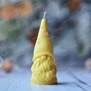 May include: A yellow candle shaped like a gnome wearing a pointed hat with stars. The candle is on a white surface.