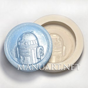 May include: A blue silicone mold with a raised design of a Star Wars R2-D2 robot. The mold is round and has a smooth surface.