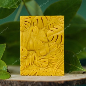 Peut inclure: Un savon jaune avec un motif détaillé d'un visage de tigre entouré de feuilles tropicales.