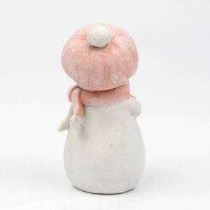 May include: A small white snowman figurine wearing a pink knit hat with a white pom pom and a pink scarf.