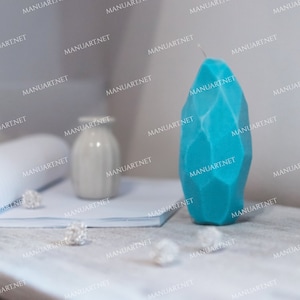 May include: A teal blue geometric candle on a white surface. The candle is shaped like a large, faceted gemstone.