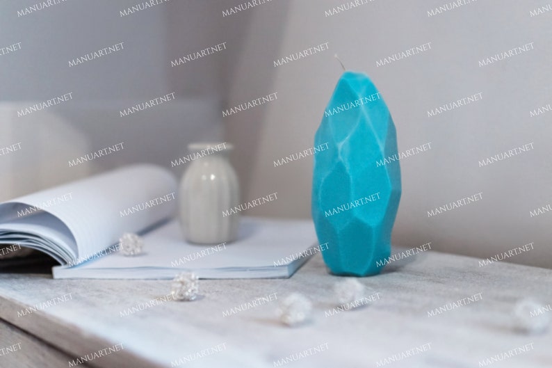 May include: A teal blue geometric candle on a white surface. The candle is shaped like a large, faceted gemstone.