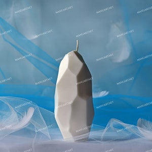 May include: A white geometric candle with a pointed top sits on a blue and white sheer fabric background.