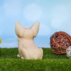 May include: A beige candle shaped like a dog sitting on a green grassy surface with brown and white wicker balls.
