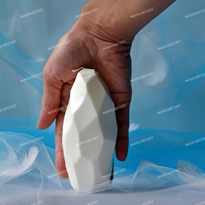 May include: A white geometric candle with a textured surface. The candle is shaped like a rounded rectangle.