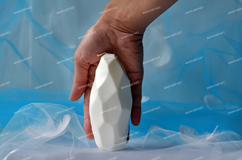 May include: A white geometric candle with a textured surface. The candle is shaped like a rounded rectangle.