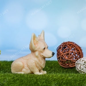 May include: A cream-colored ceramic figurine of a corgi dog sitting on a green artificial grass surface. The dog is looking to the right. There are three brown and white woven balls in the background.