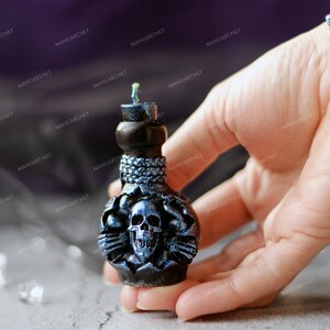 Pode incluir: Uma vela preta e azul em forma de garrafa com um design de caveira. A vela &eacute; decorada com detalhes prateados e tem um pavio preto.
