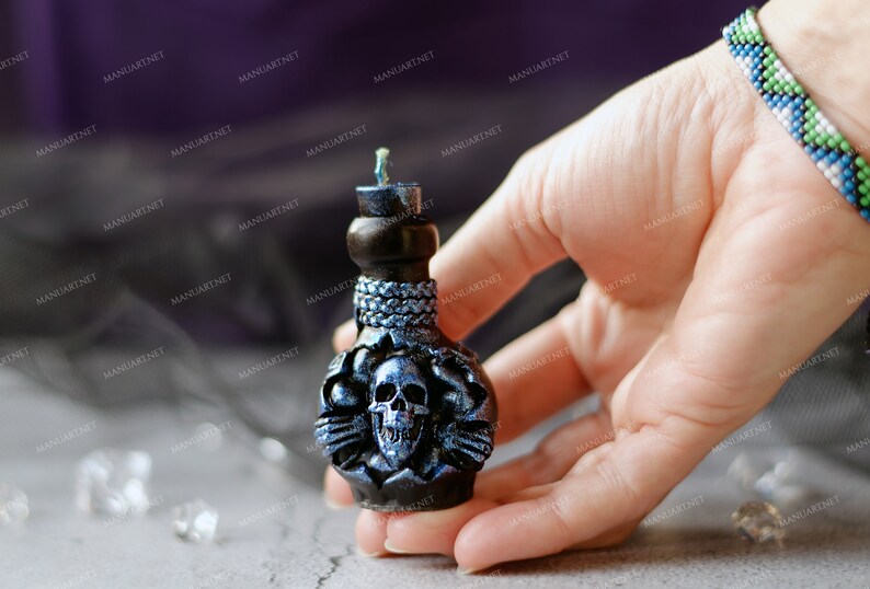 Pode incluir: Uma vela preta e azul em forma de garrafa com um design de caveira. A vela &eacute; decorada com detalhes prateados e tem um pavio preto.