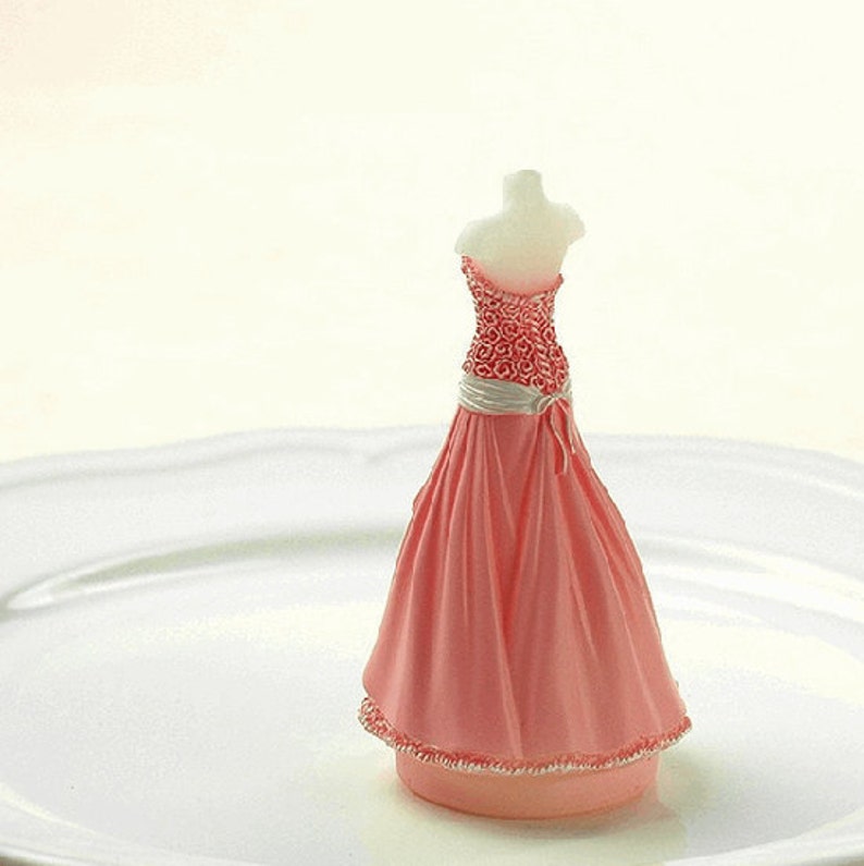 May include: A pink and white wedding cake topper featuring a bride in a pink gown with a white sash and a floral bodice.