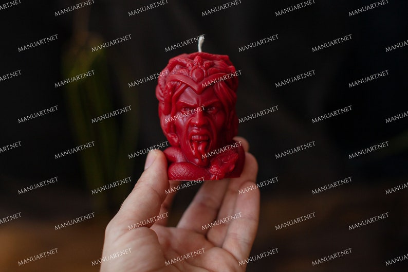 Pu&ograve; includere: Una candela rossa a forma di testa di Medusa, una figura mitologica greca con capelli di serpente. La candela ha un viso dettagliato con un'espressione feroce e una lunga lingua biforcuta.