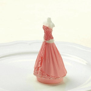 May include: A pink and white wedding cake topper featuring a bride wearing a pink gown with a white sash and floral details.