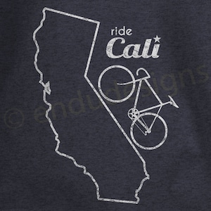May include: Dark navy blue t-shirt featuring a white outline of the state of California with a bicycle graphic. The text "ride Cali" is above the bicycle. The design has a distressed, vintage look.