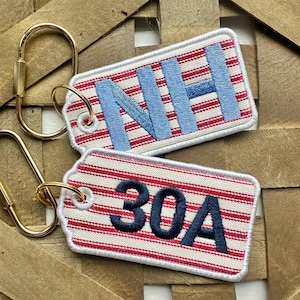 May include: Two rectangular keychains with gold-colored hardware. One keychain has the letters "NH" in light blue, and the other has the numbers "30A" in dark blue. Both keychains have a red and white striped pattern.