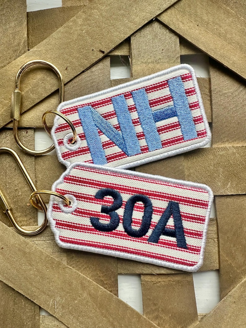 May include: Two rectangular keychains with gold-colored hardware. One keychain has the letters "NH" in light blue, and the other has the numbers "30A" in dark blue. Both keychains have a red and white striped pattern.
