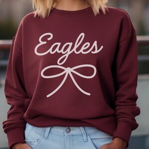 May include: Burgundy sweatshirt with white text that says "Eagles" and a white bow.