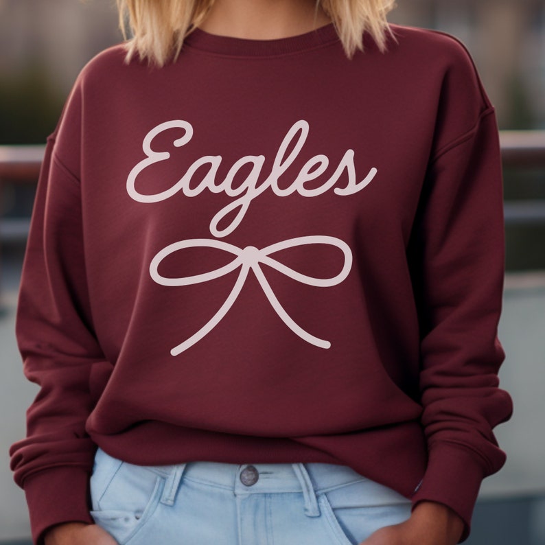 May include: Burgundy sweatshirt with white text that says "Eagles" and a white bow.
