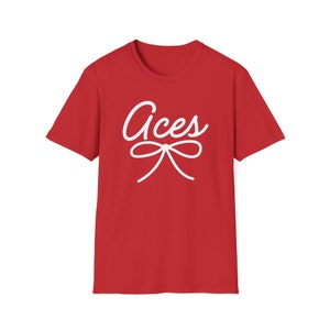 Puede incluir: Camiseta roja con texto blanco que dice "Aces" y un lazo blanco.
