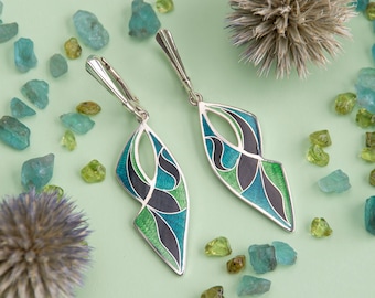 May include: A pair of silver earrings with a geometric design. The earrings are decorated with green, blue, and black enamel.