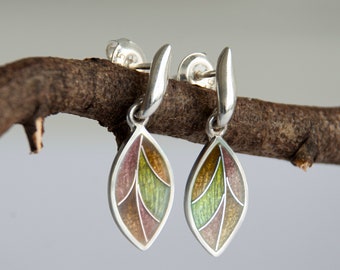 Può includere: Un paio di orecchini pendenti in argento con un design a foglia. Le foglie sono in smalto e hanno un design multicolore con sfumature di verde, marrone e rosa.