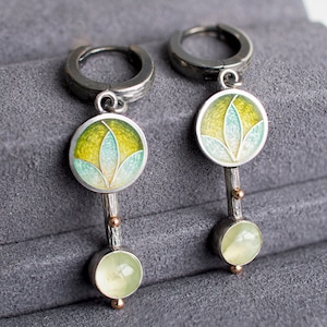 May include: A pair of silver hoop earrings with a green and yellow enamel flower design and a light green stone dangle.