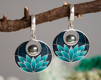 May include: A pair of silver earrings with a dark blue and teal enamel design featuring a black pearl in the center of each earring.
