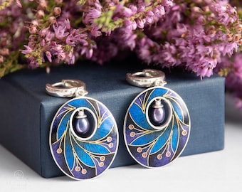 May include: A pair of silver hoop earrings with a blue and purple enamel design. Each earring features a small purple pearl in the center.