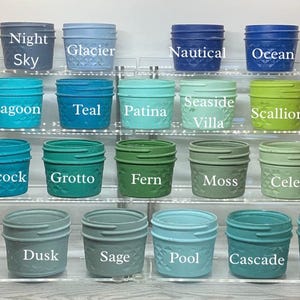 May include: A collection of small, decorative jars in various colors, including Night Sky, Glacier, Lagoon, Teal, Peacock, Grotto, Crystal, Dusk, Sage, Pool, Cascade, and Agave. Each jar has a textured pattern and a matching lid. The names of the colors are printed on the jars.