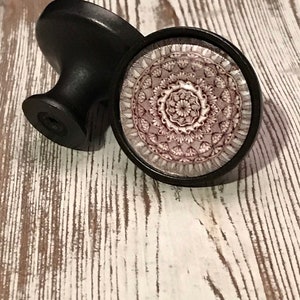 May include: Two black cabinet knobs with a mandala design. The mandala is in shades of pink and white.