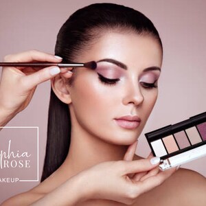 May include: A woman is applying eyeshadow with a brush. She is holding a makeup palette with a variety of shades. The palette has a black case with a silver trim. The brand name "Sophia Rose Makeup" is visible in the lower left corner of the image.