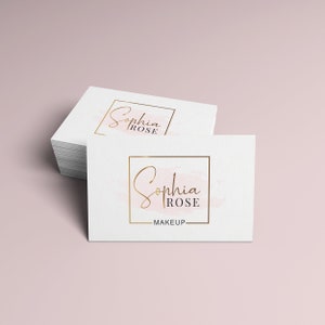 May include: Two white business cards with a gold square frame around the text "Sophia Rose Makeup". The text is in a cursive font and the background is a light pink watercolor wash.